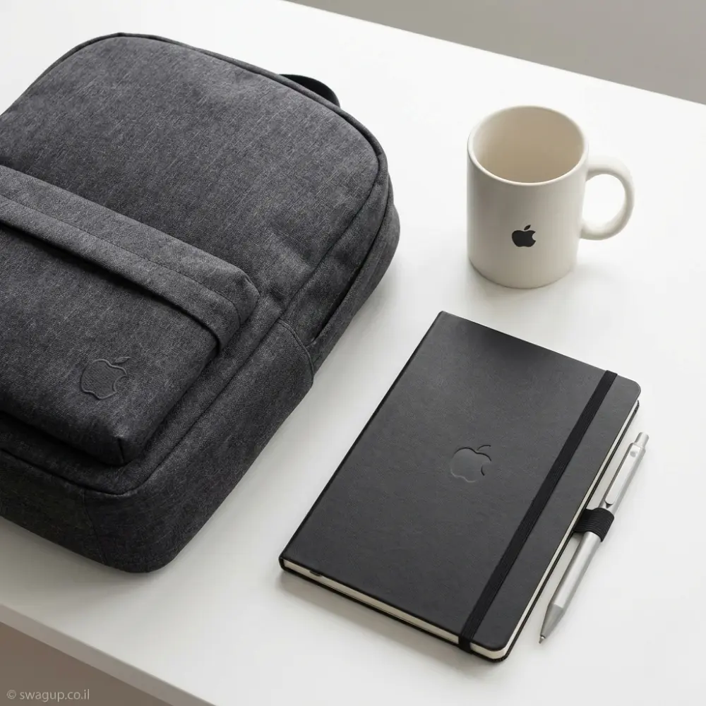 קיט מיתוג יוקרתי לעובד הכולל תיק גב אפור, מחברת שחורה, עט כסף וספל לבן על שולחן משרדי נקי.