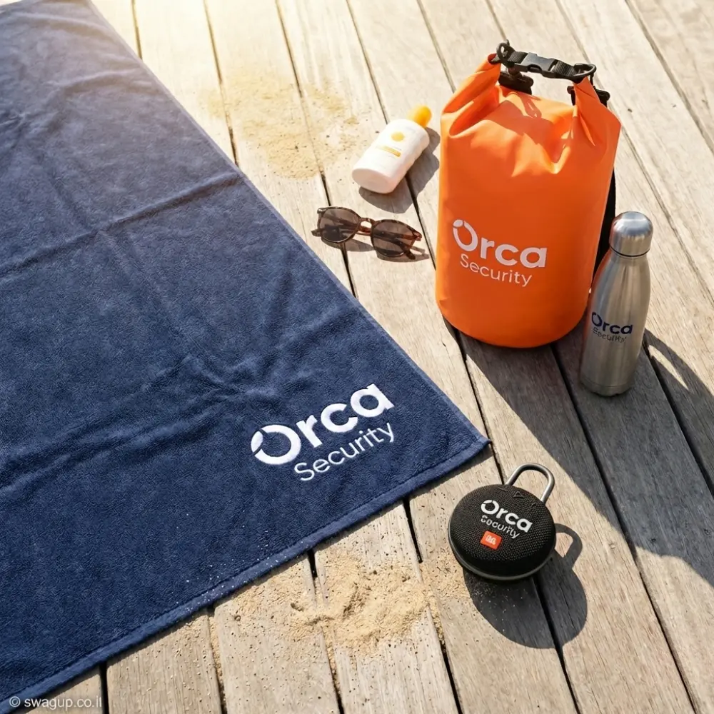 קיט מיתוג לאימונים ולים של Orca Security הכולל תיק Dry Bag כתום, מגבת כחולה, רמקול JBL ובקבוק כסוף על דק עץ.