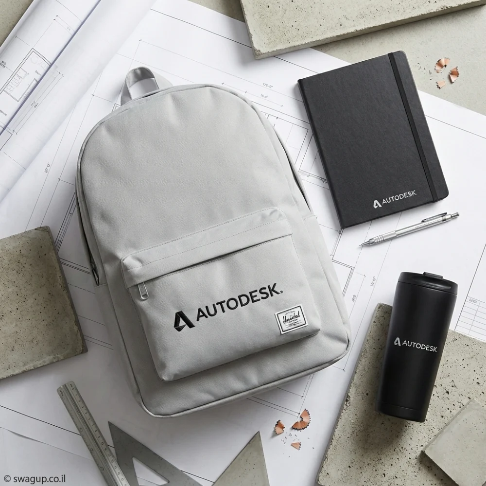 קיט מיתוג מקצועי לעובדים הכולל תיק גב אפור, מחברת שחורה, עט כסף וכוס תרמית על רקע תוכניות אדריכליות.